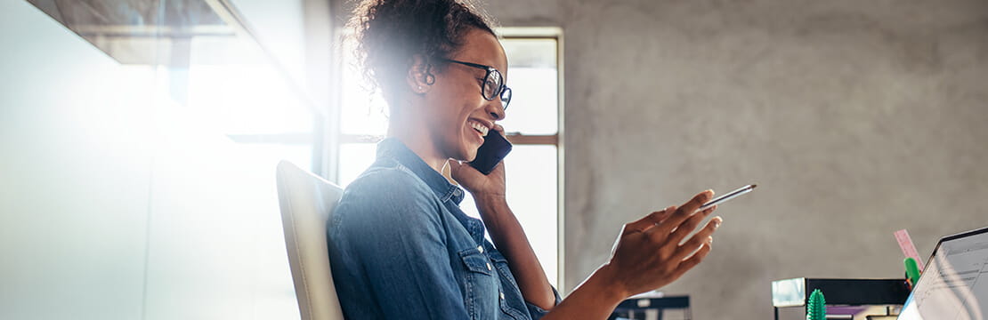 Smiling young woman talking on phone with a laptop in front.